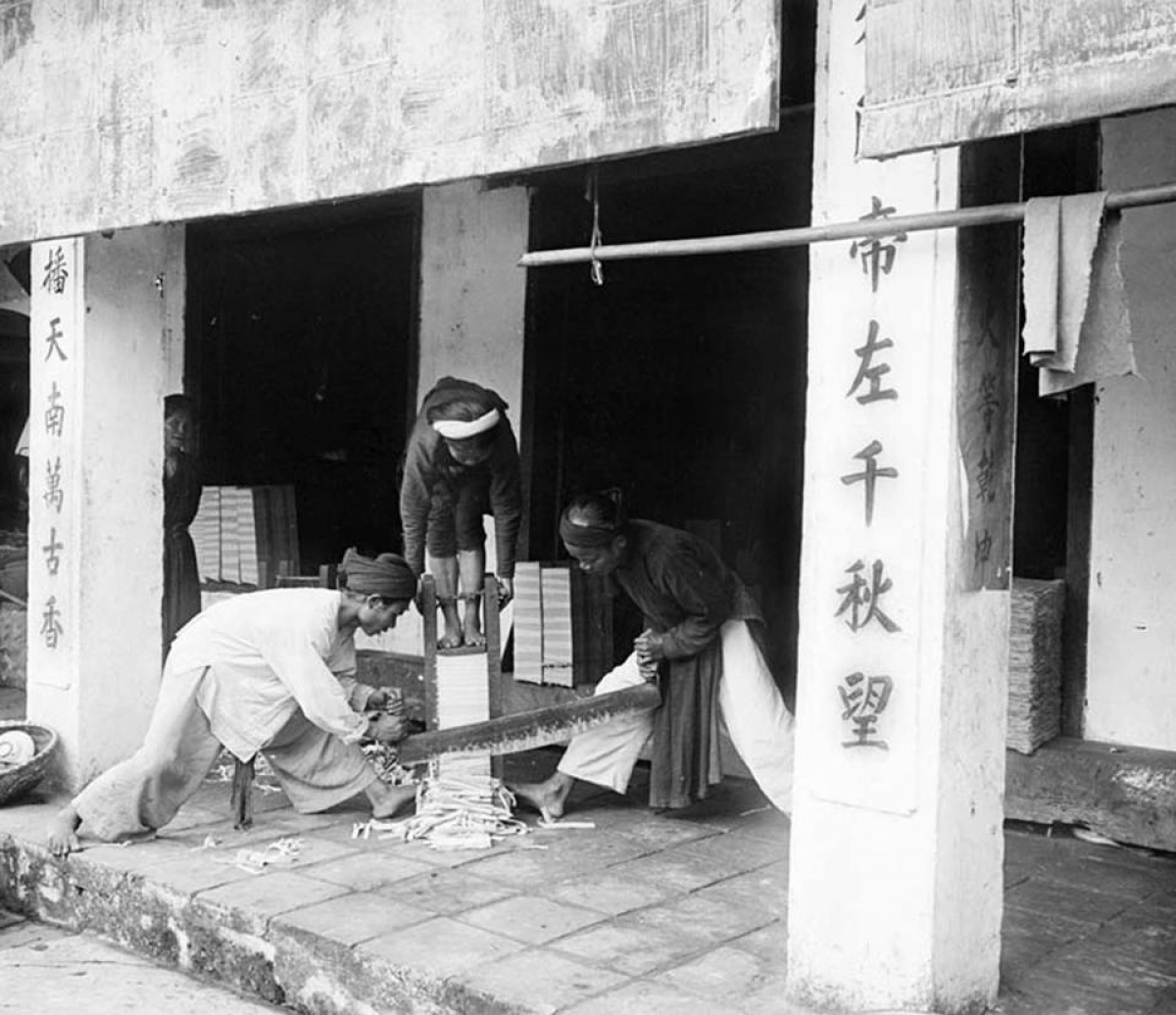 Cảnh xén đóng sách trong đền Ngọc Sơn. Một phụ nữ ép chồng sách xuống và hai nam giới xén các trang giấy.
 