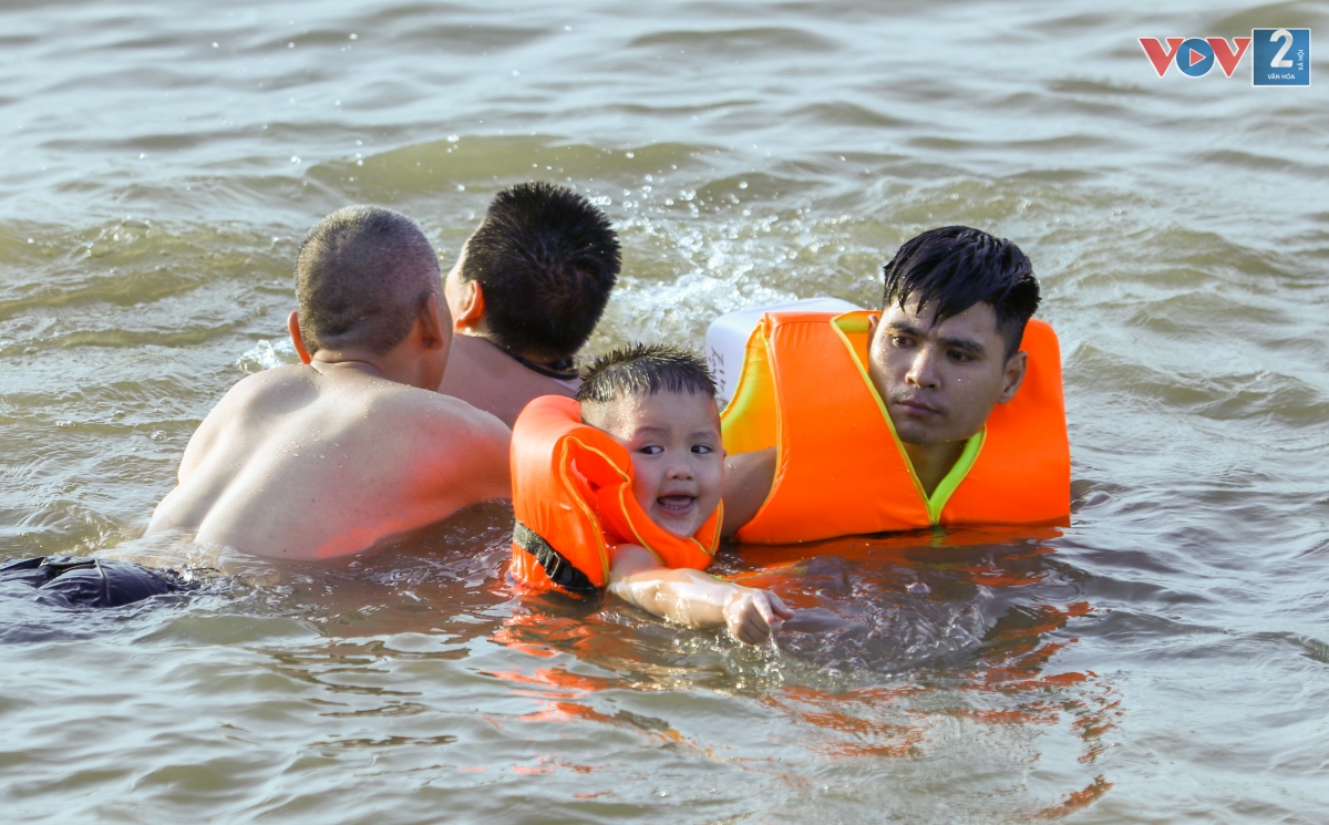 Người lớn cho trẻ nhỏ mặc áo phao và giám sát trong lúc chơi đùa dưới làn nước sông Hồng mát mẻ.