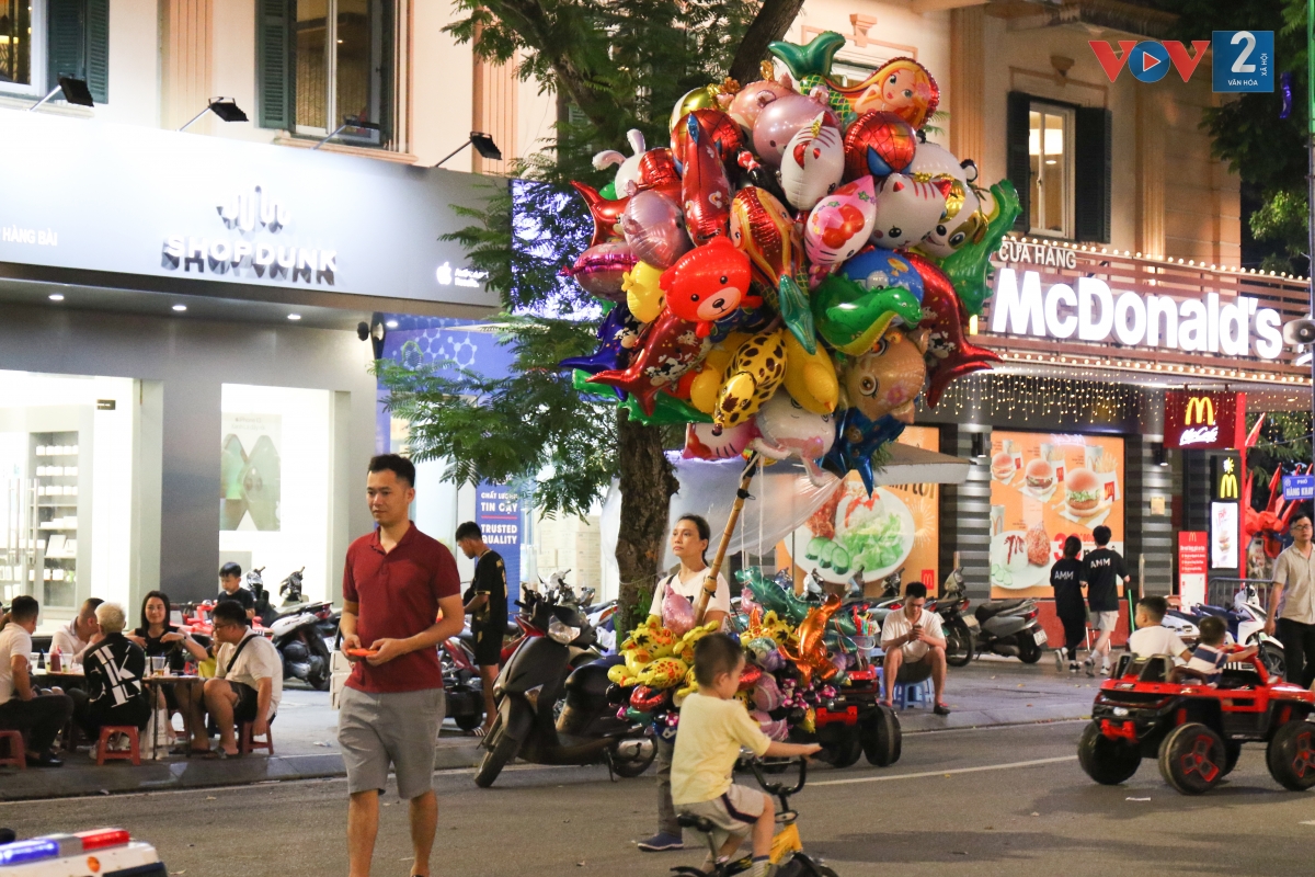Người bán bóng bay với cây gậy buộc hàng chục quả bóng to trên phố đi bộ.
