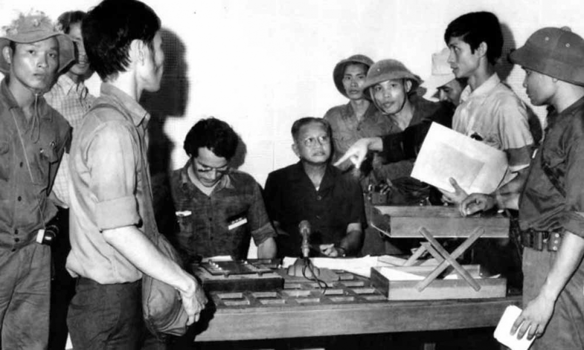 Tổng thống chính quyền Việt Nam Cộng hoà Dương Văn Minh (áo đen, ngồi) thời điểm đọc tuyên bố đầu hàng không điều kiện tại Đài Phát thanh Sài Gòn trưa 30/4/1975. Ảnh: Kỳ Nhân