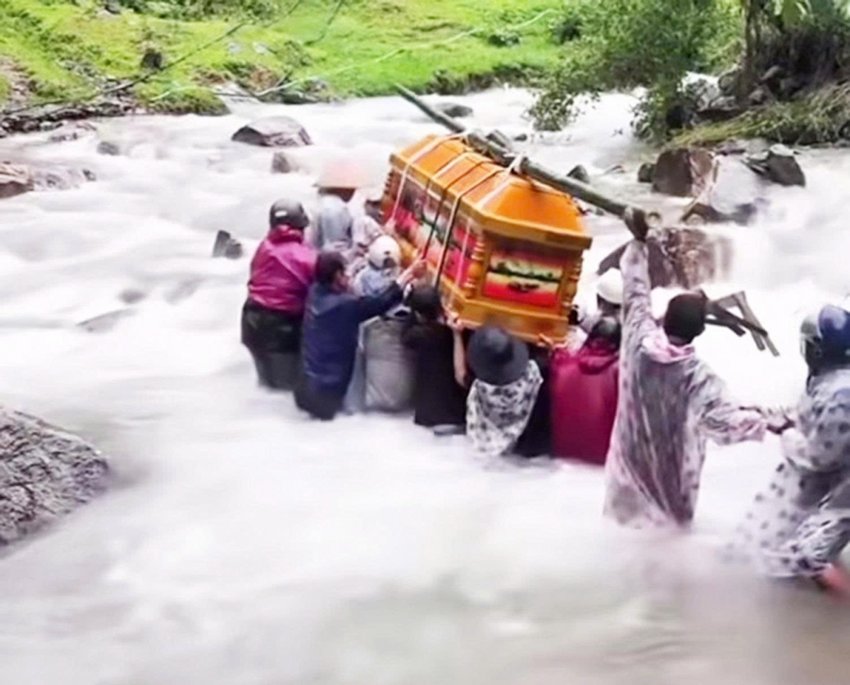 Đoàn người mặc áo mưa, chung tay khiêng chiếc quan tài, dò dẫm từng bước để băng qua dòng nước suối đang chảy xiết, cố gắng giữ thăng bằng để quan tài không bị nghiêng.