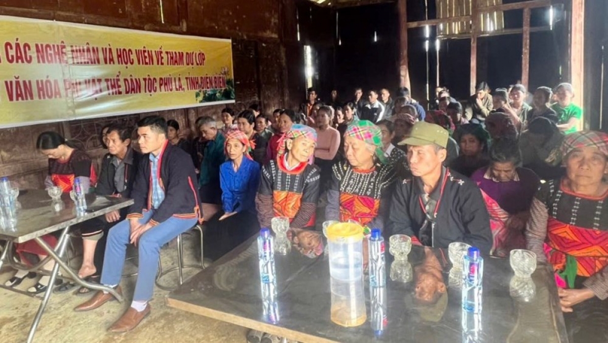 Đông đảo người dân địa phương tham gia lớp tập huấn. Trên phông nền có in logo của Bộ Văn hóa, Thể thao và Du lịch (Cục Văn hóa các dân tộc Việt Nam) và UBND tỉnh Điện Biên, cùng dòng chữ "Lớp tập huấn bảo tồn - truyền dạy văn hóa phi vật thể về Lễ Quét làng của dân tộc Phù Lá tại tỉnh Điện Biên". Nguồn: Ảnh do đơn vị tổ chức cung cấp.