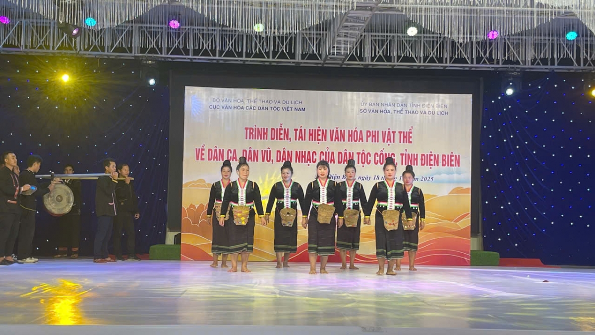 Các nghệ nhân nữ mặc trang phục truyền thống dân tộc Cống, đeo gùi nhỏ đặc trưng, đứng nghiêm trang trên sân khấu, chuẩn bị cho tiết mục biểu diễn . Phía sau, một nhóm nghệ nhân nam đang mang các nhạc cụ truyền thống. Nguồn: Ảnh do đơn vị tổ chức cung cấp.