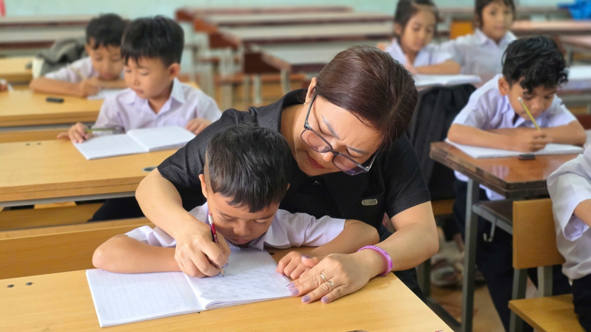 Giáo viên kèm học sinh tập viết tại lớp. Ảnh: Hoàng Qui